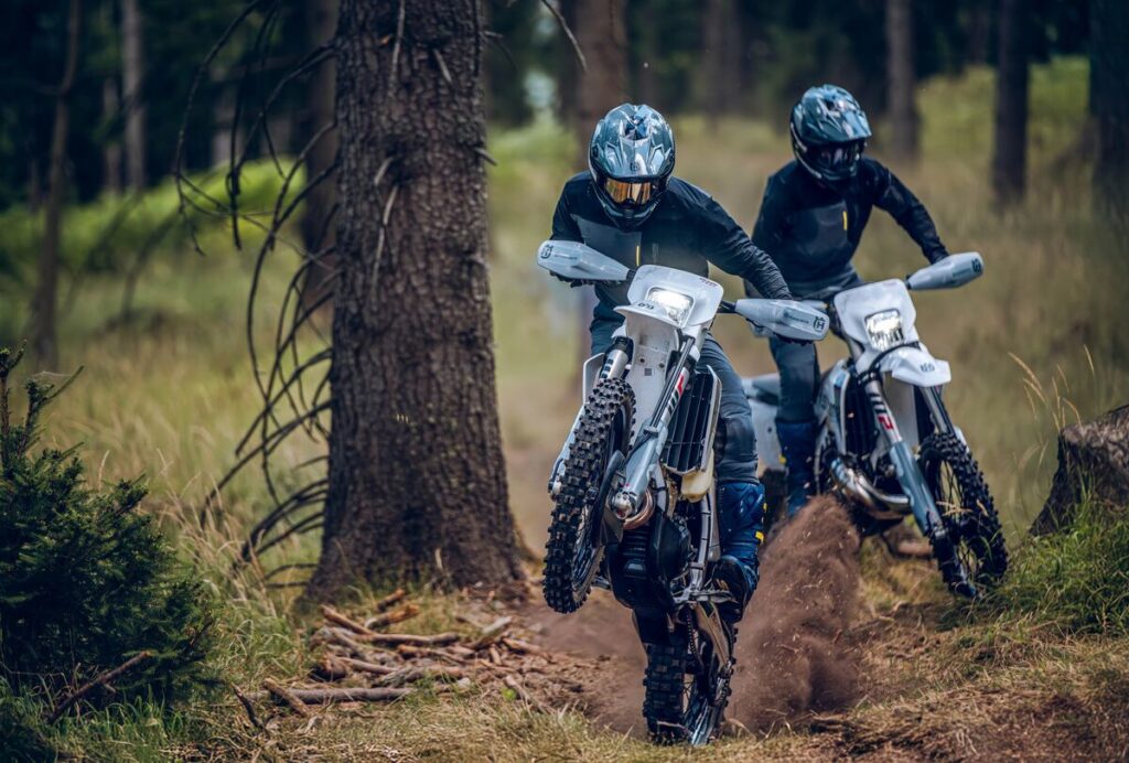 Husqvarna’s 2027 TE300 Pro and FE350 Pro riding on a dirt track with a forest backdrop.