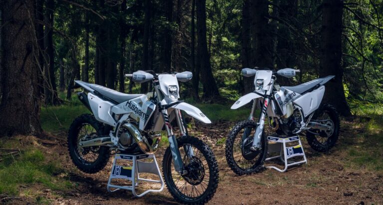 A Husqvarna TE300 Pro and an FE350 side by side in a forest.